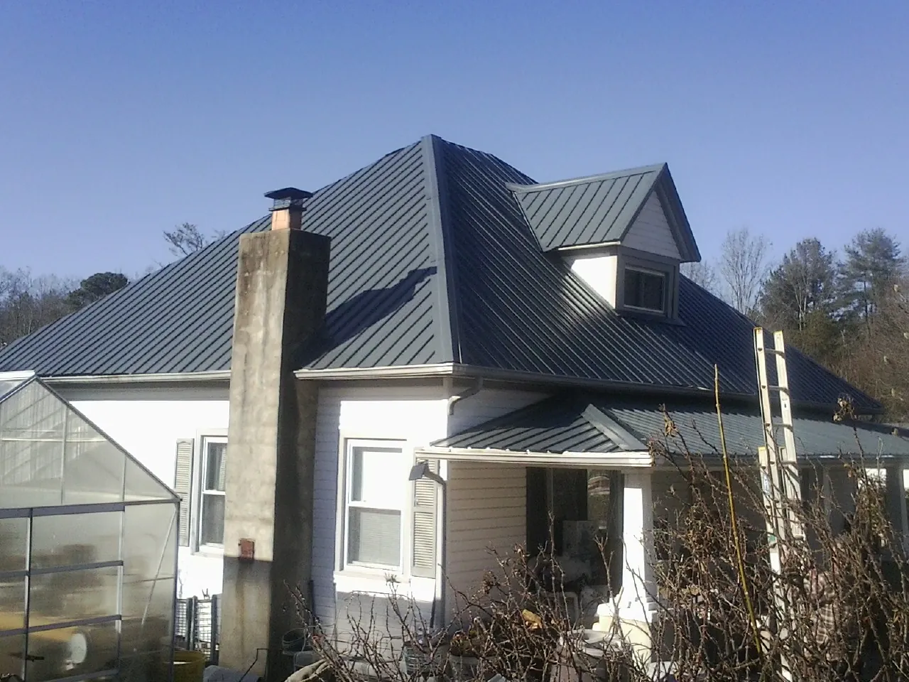Dark blue standing seam metal roof on a white farmhouse with dormer — Slate & Tile Roof Repair by Roofing Brothers in Nebraska City