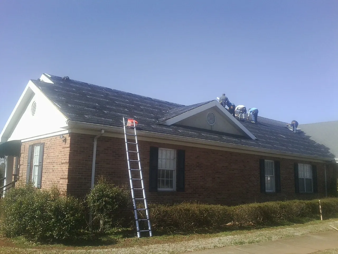 Crew tearing shingles off a brick ranch roof with a ladder set — Emergency Roof Repair work by our crew in Nebraska City