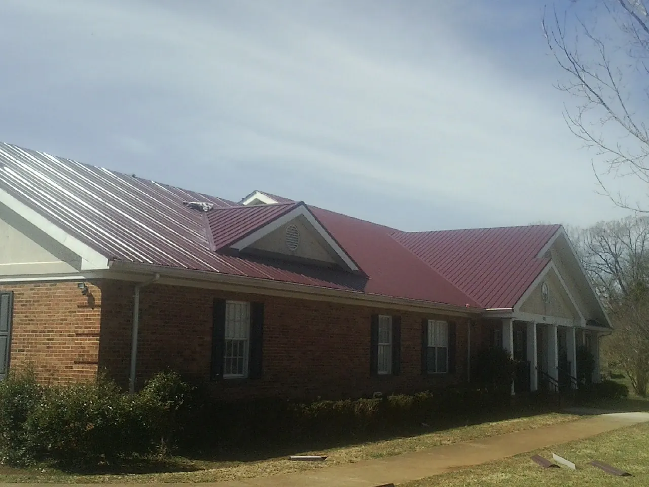 Red metal roof with gabled entries on a long brick building, from a Hail Damage Roof Repair job in Nebraska City