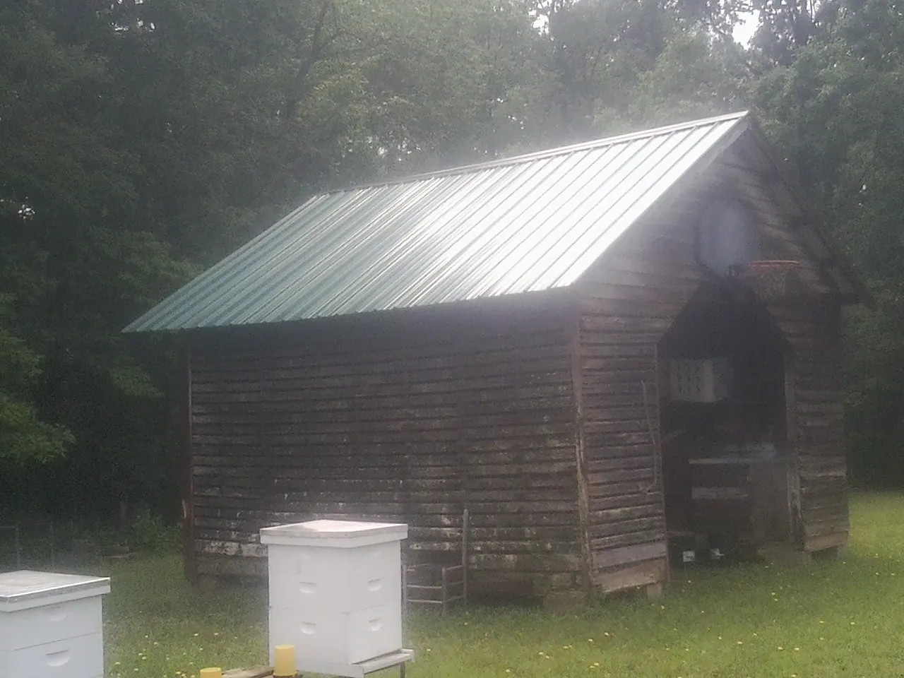 Green metal roof on a weathered barn beside stacked beehives in Nebraska City