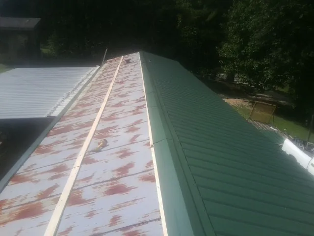 Old rusted panels beside newly installed green metal roofing — Wind Damage Roof Repair by Roofing Brothers in Nebraska City