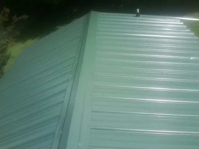 New green metal panels meeting at the ridge of a roof — Flat Roof Repair work by our crew in Nebraska City