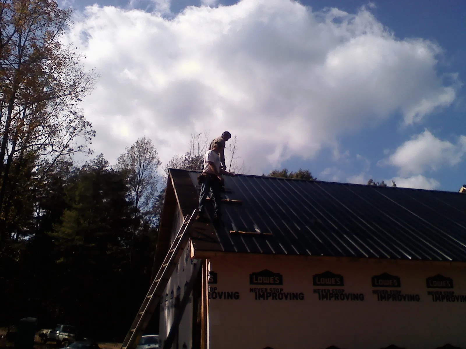 Roofer fastening dark metal panels high against a cloudy sky, from a Roof Inspection job in Nebraska City
