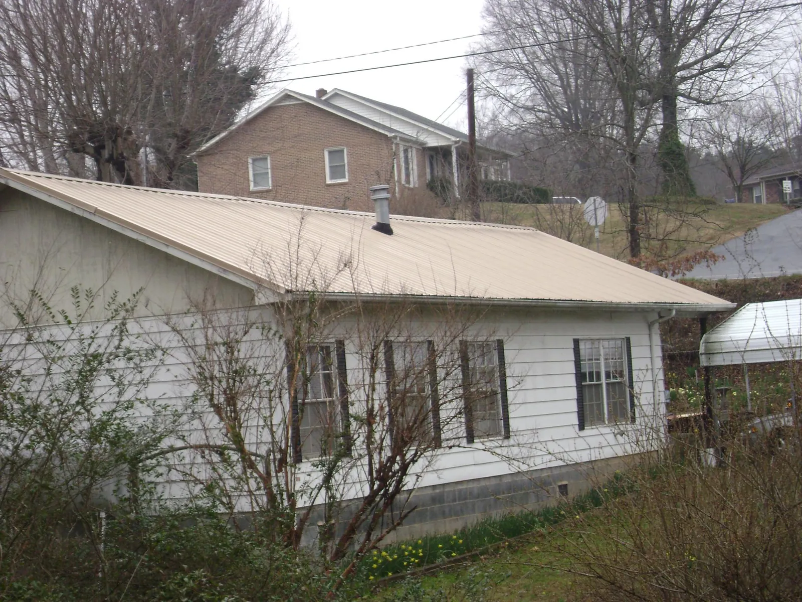 Tan metal roof on a white sided house set into a hillside — Commercial Roofing by Roofing Brothers in Nebraska City